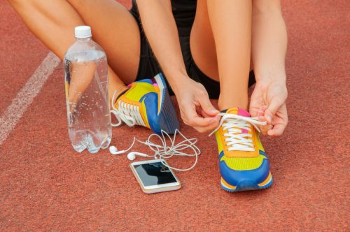 Sports woman runner tying shoelaces. Woman lacing her sneakers on a stadium running track. Workout concept
